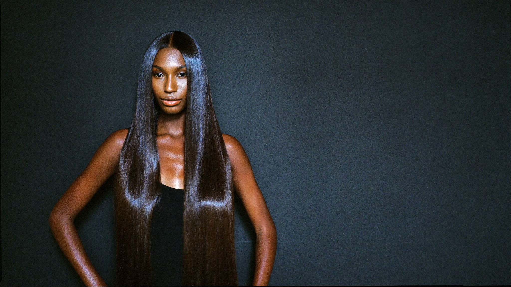 Model wearing long straight bundles at full length, against a charcoal backdrop
